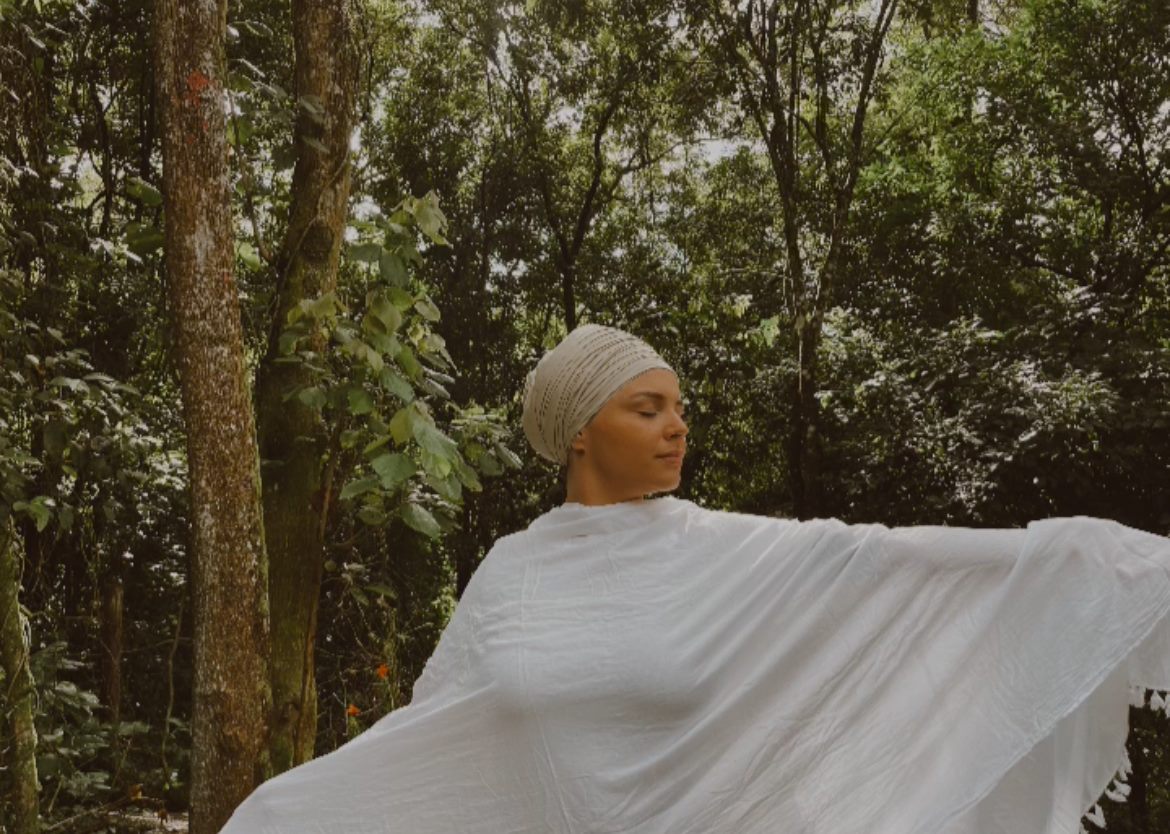 Prem Ras Kaur ao ar livre com os braços abertos e um tecido branco ao vento