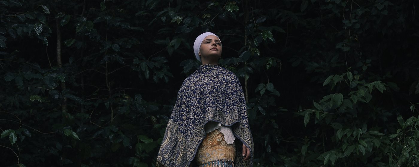 Prem Ras Kaur de pé, postura firme, em uma clareira na mata