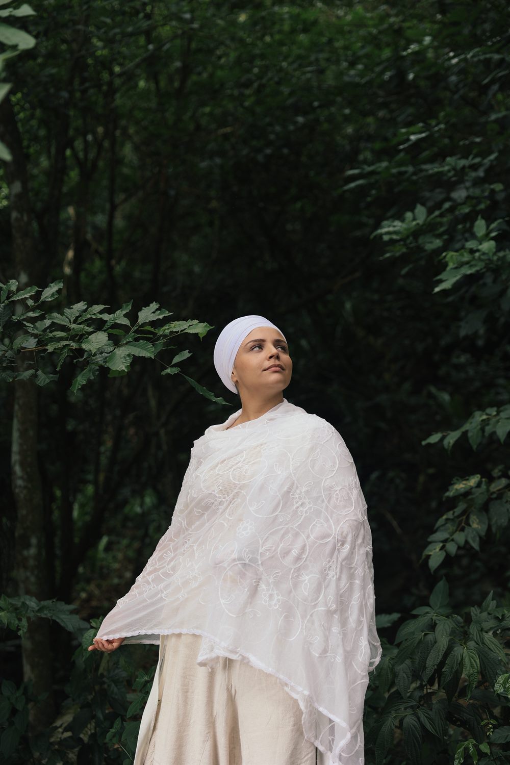 Prem Ras Kaur de pé, enraizada, olhando para a luz entre as árvores